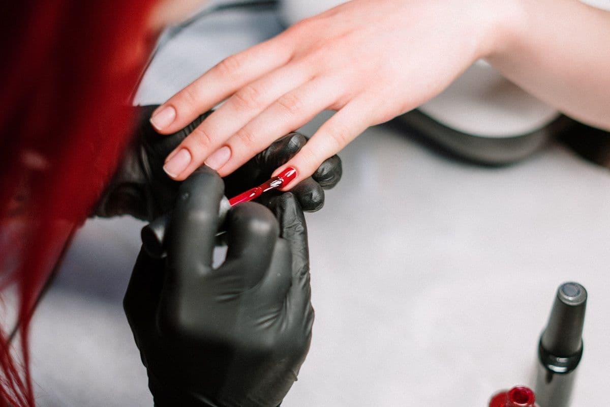 Prothésiste ongulaire en train de poser du vernis rouge sur une cliente
